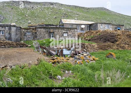 Casa in pietra in una zona rurale circondata da verdi colline e rocce, sterco di mucche di fronte, Ardenis, provincia di Shirak, Armenia Foto Stock