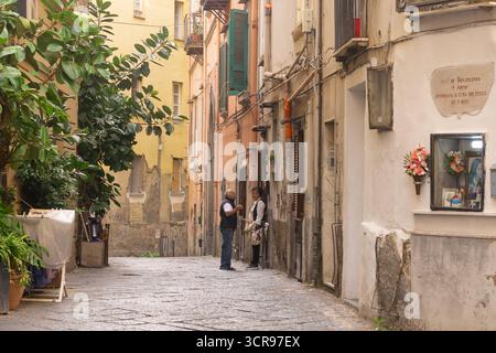 Uomo e donna in piedi in una stretta via acciottolata a Napoli con un santuario votivo stradale tradizionale (edicola votiva), Italia. Foto Stock