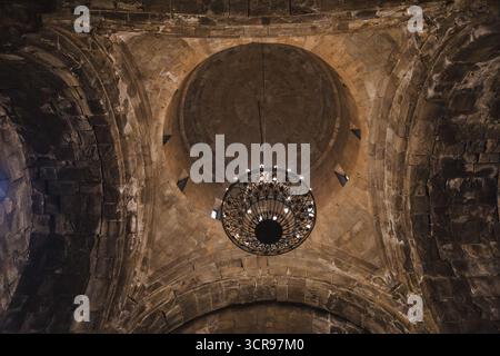 Vista del lampadario decorato appeso al soffitto a cupola in pietra nel monastero di Tatev, che getta ombre sulle mura antiche, il monastero di Tatev, la provincia di Syunik, Armenia. Foto Stock