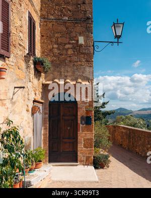 Vista di edifici in pietra soleggiati con porte in legno che si stagliano con orgoglio su un cielo azzurro, mentre un lampione proietta un caldo bagliore a Pienza, in Toscana Foto Stock