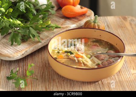 Minestrone tradizionale italiano con verdure, salsiccia e pasta, servito in una ciotola di argilla su tavola di legno. Cibo e stile di vita sano Foto Stock