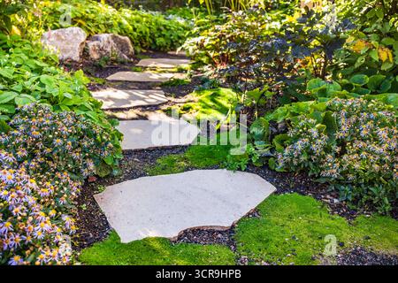 Sentiero con grandi lastre di pietra attraverso un giardino splendidamente piantato Foto Stock