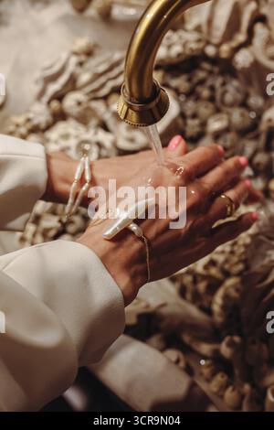 In un bagno elegante, una giovane donna con le perle alla moda si lava le mani in un lavandino a conchiglia splendidamente decorato. La scena è in mostra Foto Stock
