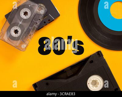 Audiocassetta vintage, disco in vinile e videocassetta VHS che rappresentano gli anni ottanta su sfondo giallo Foto Stock
