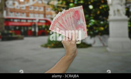 Mano maschile che tiene in mano più banconote da 50 peso in un ambiente urbano all'aperto con sfondo urbano sfocato, enfatizzando i concetti valutari e finanziari. Foto Stock