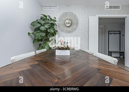 Sala da pranzo rustica con un tavolo in quercia e sedie in vimini, illuminata da un lampadario sospeso in ferro battuto Foto Stock