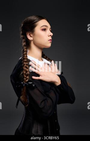 Una ragazza in treccia indossa un abito gotico, fingendosi un personaggio serio del mercoledì. Foto Stock