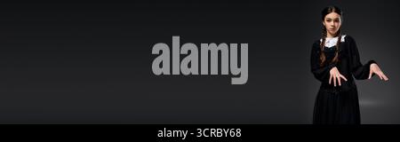 Una ragazza in treccia indossa un abito gotico del mercoledì, abbracciando lo spirito spettrale di Halloween, lo striscione Foto Stock