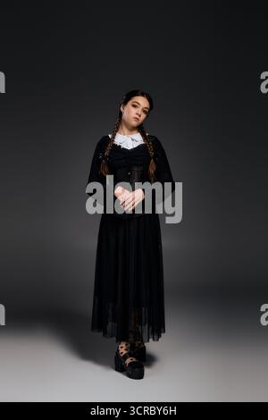 Una ragazza con un abito gotico mercoledì con trecce si posa elegantemente durante la stagione di Halloween. Foto Stock