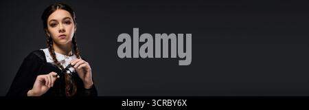 La ragazza con trecce indossa un abito in stile gotico del mercoledì ispirato a un personaggio spaventoso amato, uno striscione Foto Stock