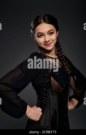 Una ragazza con trecce indossa un abito gotico mercoledì e sorride mentre celebra Halloween. Foto Stock