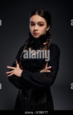 Una ragazza seria in costume gotico mercoledì posa con trecce, abbracciando lo spirito di Halloween. Foto Stock