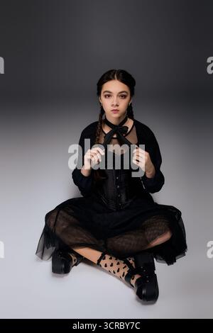 Una ragazza vestita in stile gotico il mercoledì si siede tranquillamente, abbracciando l'atmosfera autunnale di Halloween. Foto Stock