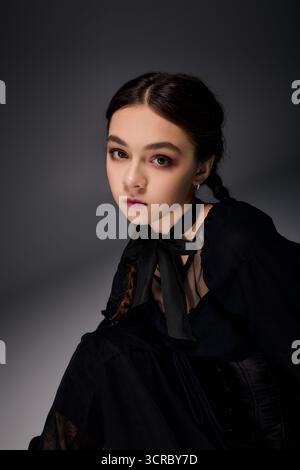 Una ragazza con trecce indossa un abito gotico del mercoledì, catturando l'essenza dello spirito di Halloween. Foto Stock