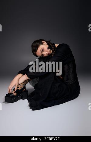 Un bambino con trecce seduto con grazia in un abito scuro del mercoledì, catturando l'essenza di Halloween. Foto Stock