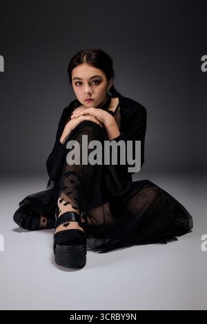 Una ragazza con trecce si siede graziosamente con un abito scuro del mercoledì, perfetto per le feste di Halloween. Foto Stock