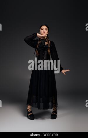Una ragazza con trecce posa in un abito gotico del mercoledì per Halloween, mostrando il suo carattere spettrale. Foto Stock
