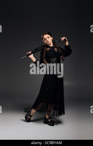 Una ragazza con le trecce è vestita con un costume gotico del mercoledì, canalizzando un'atmosfera spettrale. Foto Stock