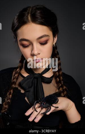 La ragazza con trecce indossa un abito gotico, che incarna un personaggio spaventoso del mercoledì con un ragno Foto Stock