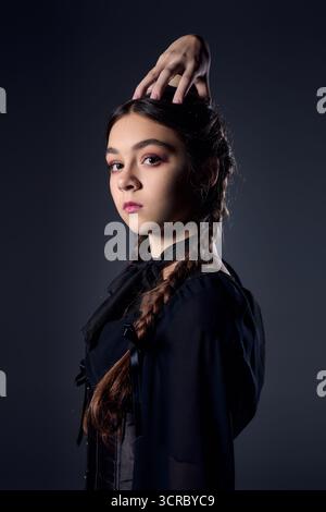 Una ragazza con trecce si posa in un abito gotico scuro del mercoledì, catturando l'essenza di Halloween. Foto Stock