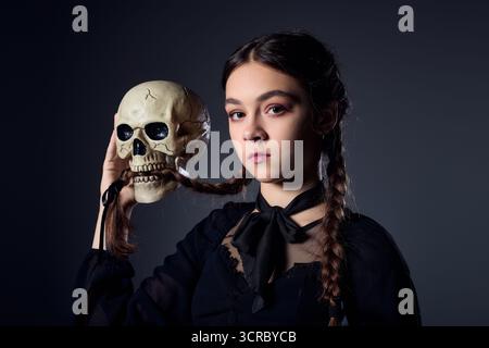 La ragazza con i capelli intrecciati indossa un abito gotico mentre tiene in mano un teschio, mercoledì Foto Stock