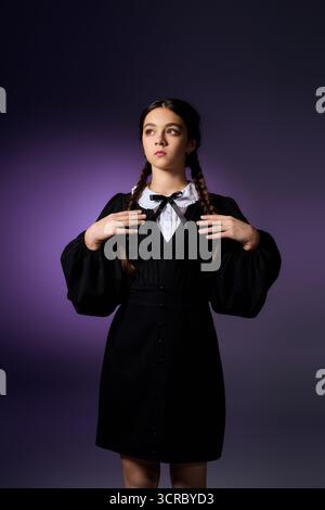 Una ragazza con trecce si posa in un abito gotico, incarnando l'essenza del mercoledì per Halloween. Foto Stock