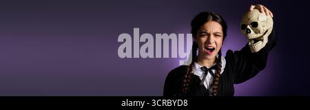 La ragazza con trecce indossa un abito in stile gotico mentre tiene in mano un teschio per il divertimento di Halloween, striscione Foto Stock