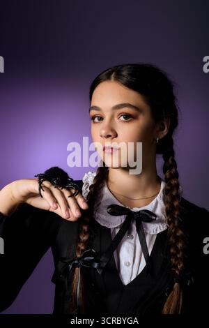 Bambino vestito come un personaggio gotico del mercoledì con trecce, che mostra un ragno per il divertimento di Halloween. Foto Stock