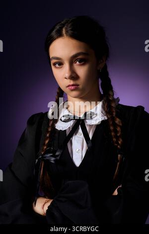 Una ragazza con trecce si posa in un abito gotico, incarnando il personaggio di mercoledì per Halloween. Foto Stock