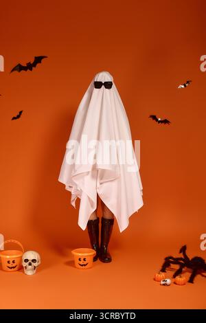 Un bambino in costume da fantasma celebra Halloween con uno sfondo arancione. Foto Stock