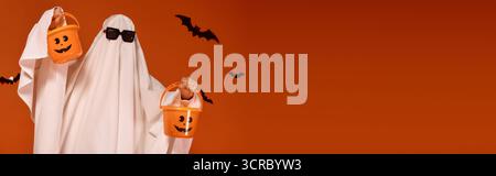 Un bambino in costume da fantasma celebra con gioia Halloween con un arredamento spettrale intorno a lei, banner Foto Stock