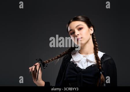 Una ragazza con trecce indossa un abito gotico di mercoledì, incarnando un personaggio spaventoso per Halloween. Foto Stock