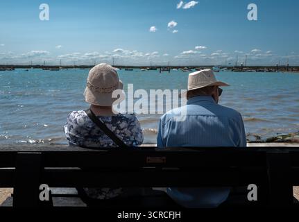 una vecchia coppia in cappello, seduta sulla panchina, che guarda dall'altra parte dell'acqua, Foto Stock