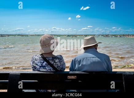 una vecchia coppia in cappello, seduta sulla panchina, che guarda dall'altra parte dell'acqua, Foto Stock