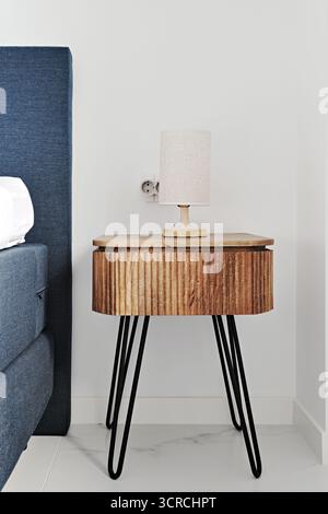 Interni della camera da letto con elegante comodino in legno, scanalature verticali e eleganti gambe in metallo nero. Design moderno di ispirazione scandinava. Ho alloggiato in stile contemporaneo Foto Stock