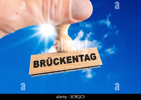 Baviera, Germania - 30 settembre 2025: FOTOMONTAGGIO, mano con timbro di legno e iscrizione: Brückentag *** FOTOMONTAGE, hand mit einem Holzstempel und der Aufschrift: Brückentag Foto Stock