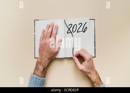 Open planner con 2026, inserimento manuale di un segnalibro: Simbolo di voltare pagina, nuovo inizio, risoluzioni, pianificazione e organizzazione personale. Foto Stock