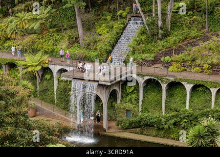 I turisti apprezzano i giardini panoramici a strati e la cascata con vegetazione lussureggiante e sentieri ad arco in un tranquillo parco in cui si trovano i Giardini del Monte Palace di Madeira Foto Stock