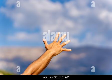 Mano umana tesa che raggiunge il cielo blu con nuvole, simboleggiando la libertà, la speranza, la gioia e l'aspirazione Foto Stock
