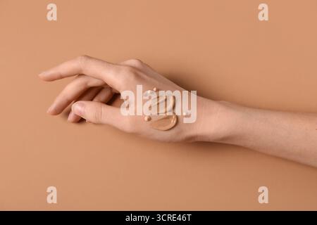 Mano femminile con campioni di base per il trucco su sfondo marrone Foto Stock