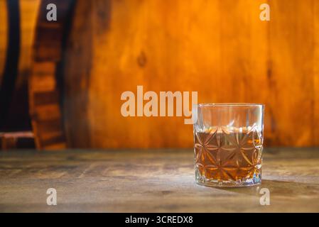Un bicchiere di alcol forte in un seminterrato scuro e polveroso con botti di rovere su un vecchio tavolo texture. Posiziona per testo Foto Stock