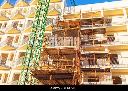 Cantiere in corso di costruzione, con un grande edificio di appartamenti in fase di costruzione, caratterizzato da un'ampia ponteggio in metallo e da una gru da costruzione. Strutture temporanee Foto Stock