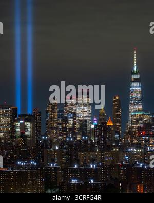 Tributo alla luce. La vista di fasci doppi luminosi perforano il cielo notturno su un vasto paesaggio urbano, riflettendo sui moderni grattacieli in solenne ricordo del 9-11, New York, New York, Stati Uniti. Foto Stock