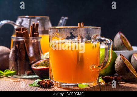 Bevanda a base di tè caldo al frutto della passione con succo di frutta, cannella, lime, su fondo di legno con frutta fresca e spezie Foto Stock