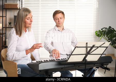 Tutore che insegna all'uomo a suonare il pianoforte al chiuso Foto Stock