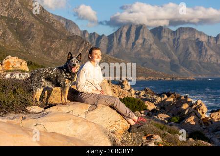 Una donna con un cane da bestiame australiano (Blue Heeler) che esplora l'oceano e le montagne Foto Stock