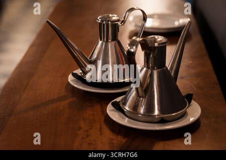 un paio di eleganti distributori di olio d'oliva in acciaio inox su un tavolo di legno in un ristorante Foto Stock
