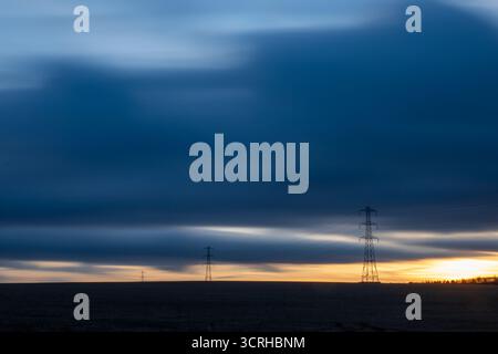 Tralicci elettrici in un paesaggio aperto all'alba con un cielo spettacolare Foto Stock