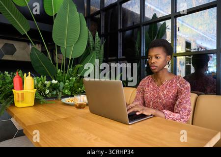 Donna afroamericana che lavora su un computer portatile in un bar Foto Stock