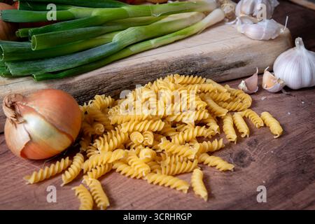 Un mucchio di pasta italiana secca Fusilli su un piano di lavoro della cucina insieme a varie verdure. Foto Stock